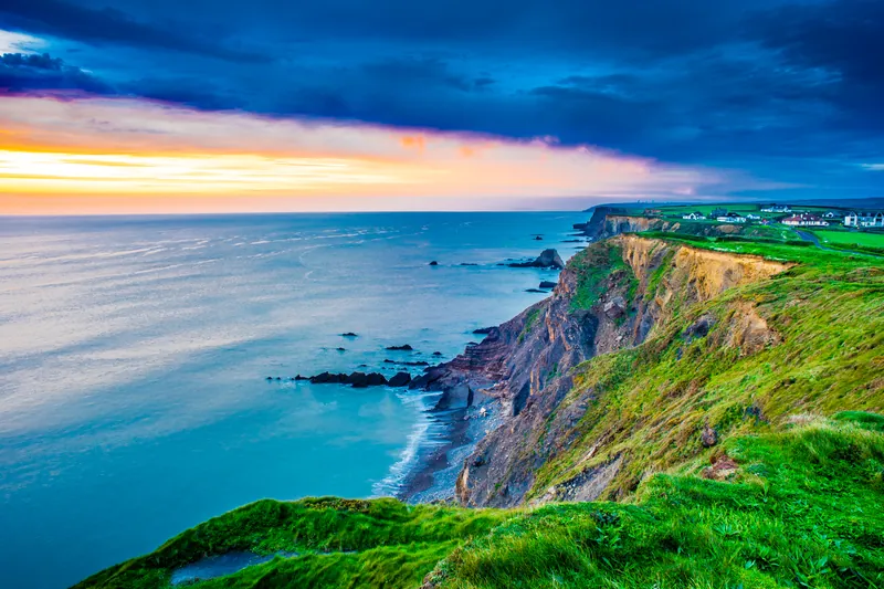 The coastline at Bude, North Cornwall, at sunset, with the town on the clifftop in the distance.